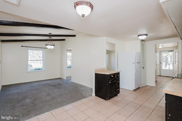 interior space featuring dark cabinetry, freestanding refrigerator, light countertops, beamed ceiling, and light colored carpet