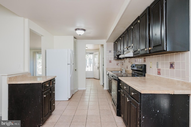 kitchen with light tile patterned floors, freestanding refrigerator, black electric range oven, dark cabinets, and backsplash