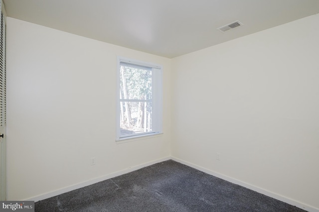 spare room with visible vents, baseboards, and dark colored carpet