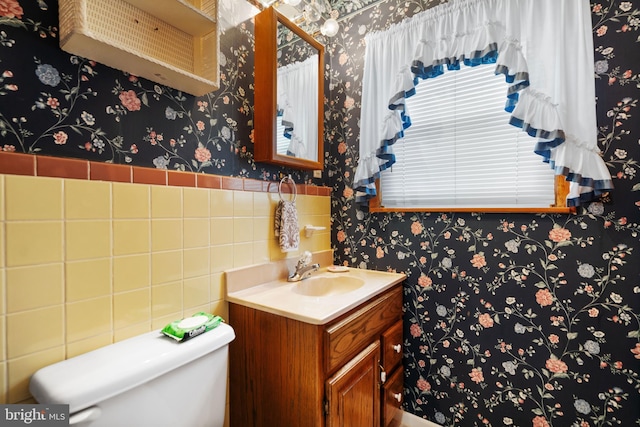 half bathroom with wainscoting, vanity, toilet, and wallpapered walls