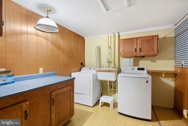 clothes washing area featuring washing machine and dryer, cabinet space, and wooden walls