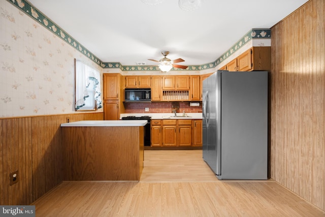 kitchen with a wainscoted wall, light countertops, light wood-type flooring, black appliances, and wallpapered walls