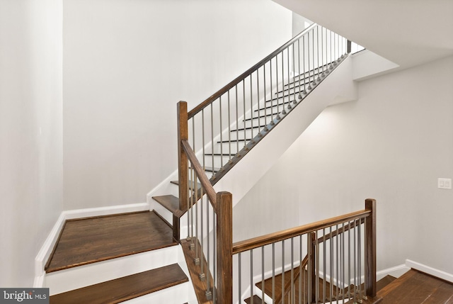 stairs with baseboards, wood finished floors, and a towering ceiling