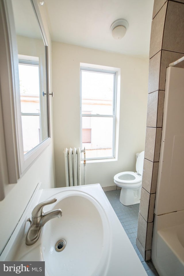 bathroom featuring tile patterned flooring, toilet, a sink, radiator, and a bathtub