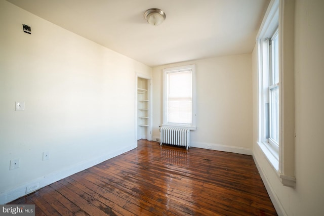 empty room with hardwood / wood-style floors, radiator heating unit, built in shelves, and baseboards