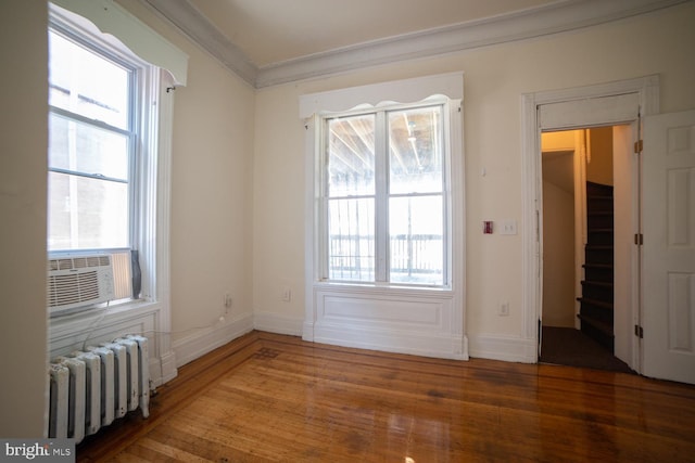 unfurnished room featuring radiator, ornamental molding, a wealth of natural light, and wood finished floors