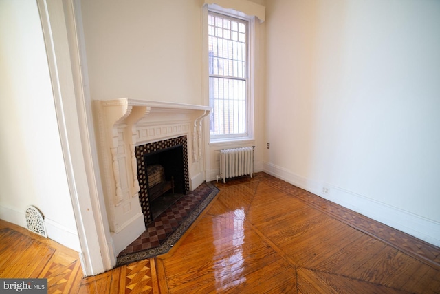 unfurnished living room featuring radiator heating unit, baseboards, and a tiled fireplace