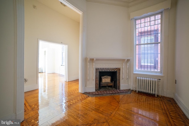 unfurnished living room featuring radiator heating unit, a tiled fireplace, wood finished floors, and baseboards