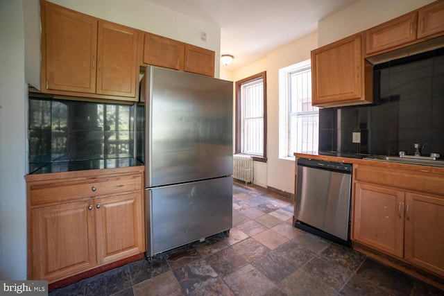 kitchen with radiator, tile countertops, stainless steel appliances, stone tile flooring, and a sink