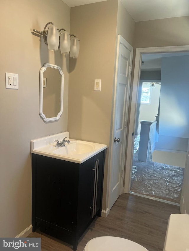 bathroom featuring baseboards, toilet, wood finished floors, and vanity