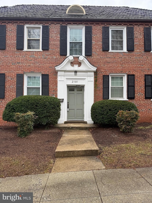 doorway to property with brick siding and roof with shingles