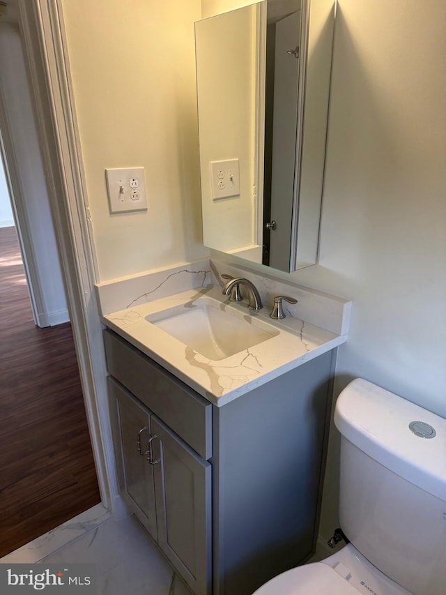 half bathroom featuring marble finish floor, vanity, and toilet