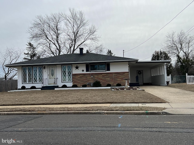 view of front of house featuring concrete driveway, stone siding, a chimney, fence, and a carport