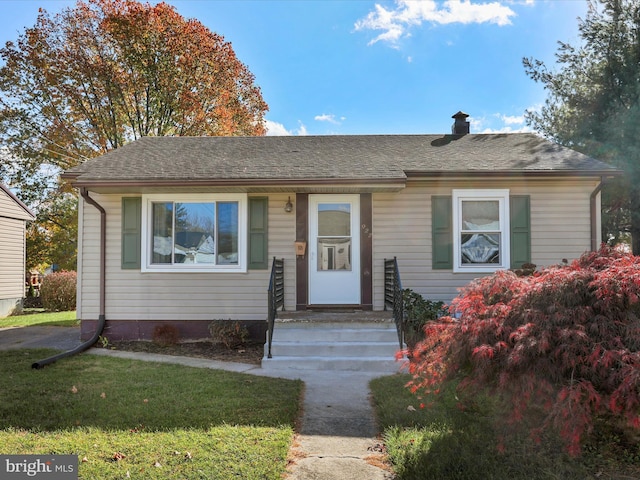 view of front of home with a shingled roof, a chimney, and a front yard