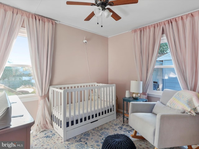 bedroom featuring a ceiling fan, a nursery area, and multiple windows