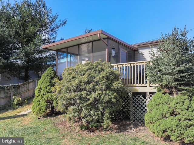 back of property with a wooden deck, a sunroom, and fence