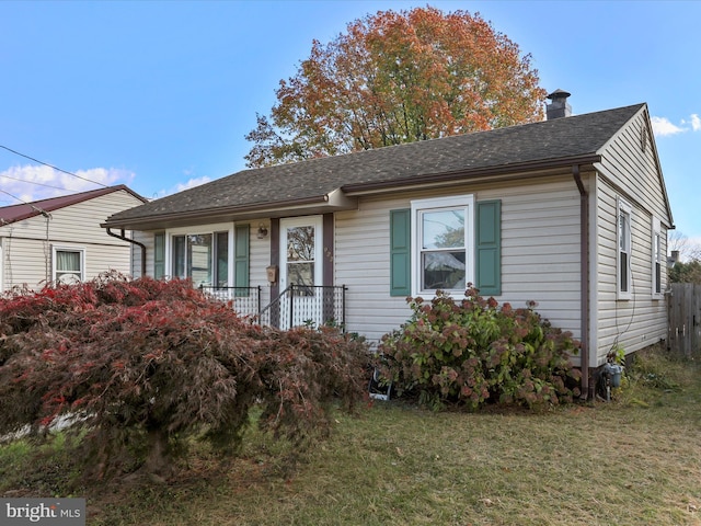 ranch-style house with roof with shingles, a chimney, and a front yard