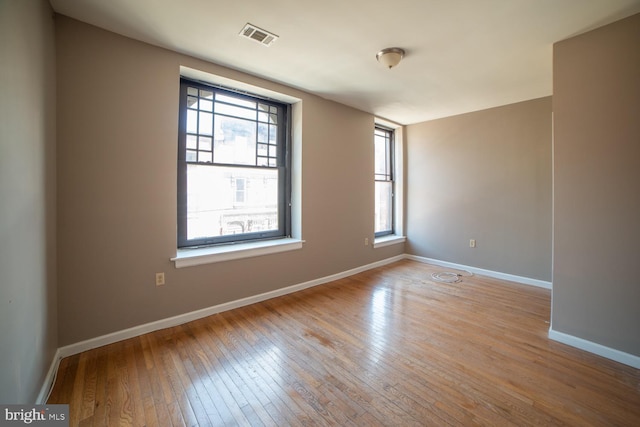 unfurnished room featuring hardwood / wood-style flooring, baseboards, and visible vents