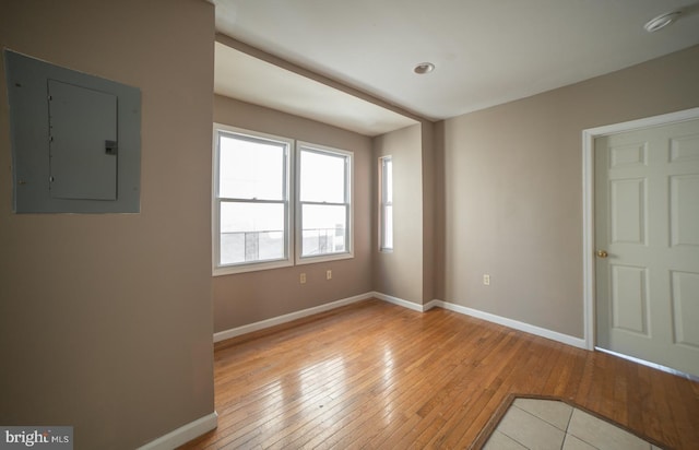 unfurnished room featuring light wood-type flooring, electric panel, and baseboards