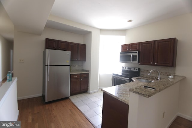 kitchen with tasteful backsplash, appliances with stainless steel finishes, a sink, light stone countertops, and a peninsula