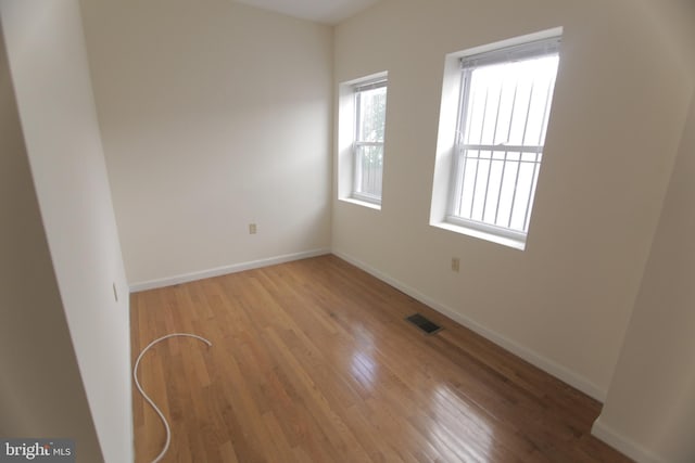 spare room with baseboards, visible vents, and wood finished floors