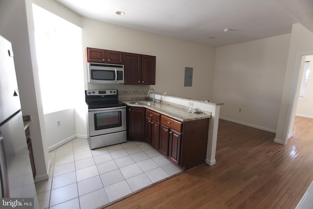 kitchen with decorative backsplash, light stone counters, a peninsula, stainless steel appliances, and a sink