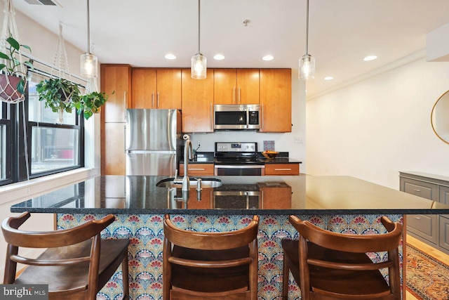 kitchen with stainless steel appliances, a sink, a kitchen breakfast bar, brown cabinetry, and decorative light fixtures