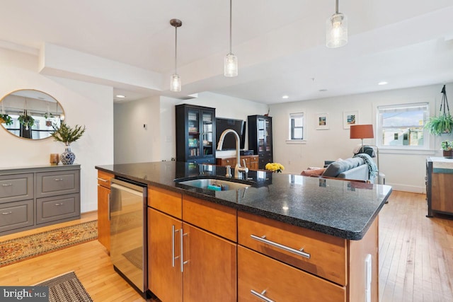 kitchen featuring light wood finished floors, open floor plan, a sink, an island with sink, and dishwasher