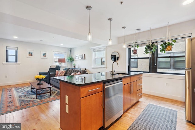 kitchen with a center island with sink, stainless steel appliances, light wood-style flooring, brown cabinetry, and a sink