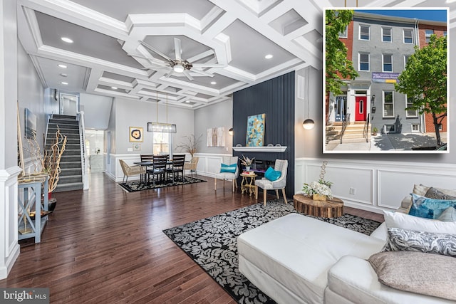 living room featuring coffered ceiling, ceiling fan, stairway, wood finished floors, and a decorative wall