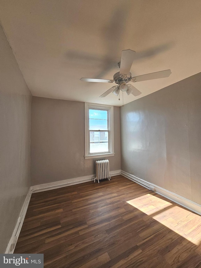 spare room featuring radiator, a ceiling fan, baseboards, and dark wood-style flooring