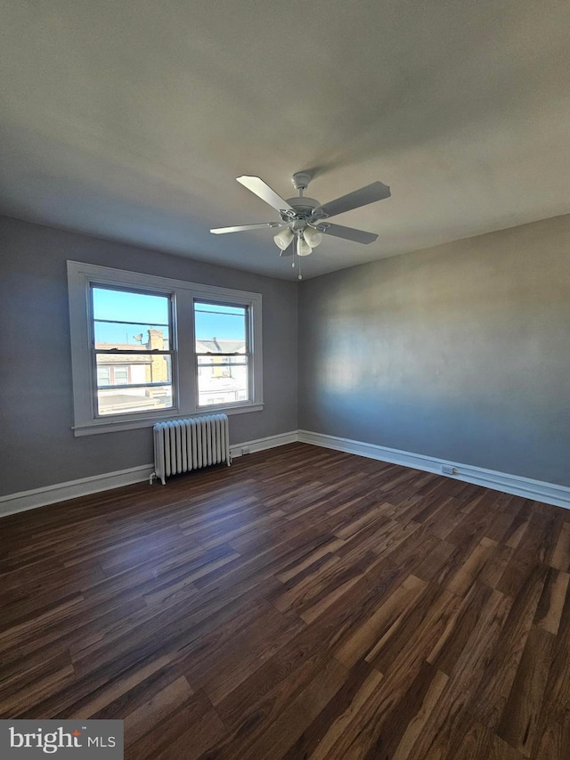 spare room featuring dark wood-style floors, baseboards, radiator heating unit, and a ceiling fan