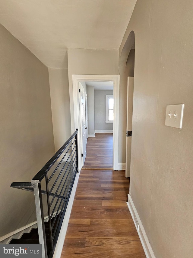 hallway with arched walkways, baseboards, and wood finished floors