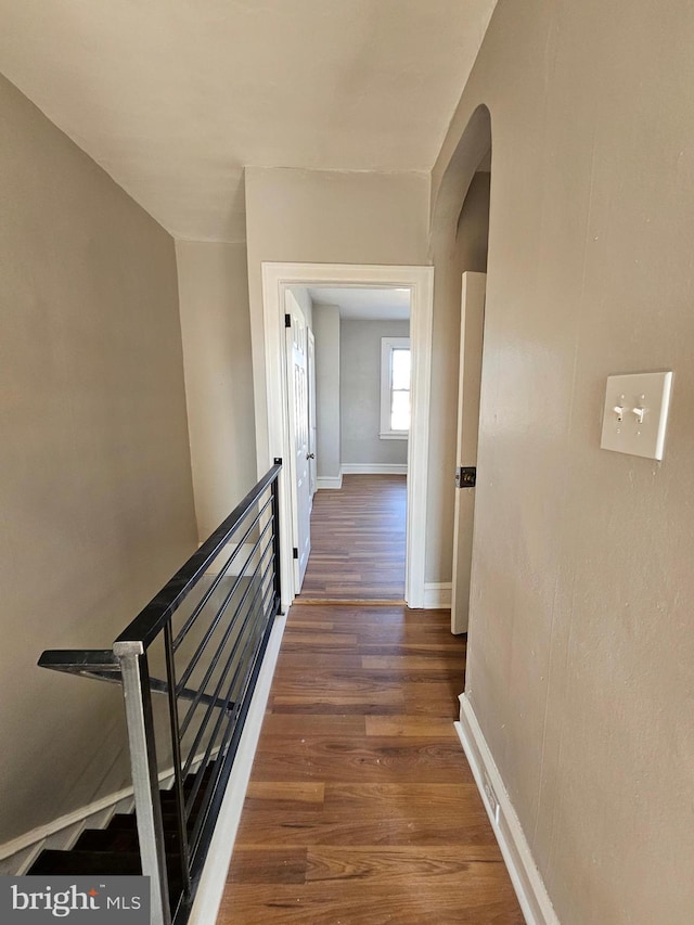 hallway with arched walkways, wood finished floors, and baseboards