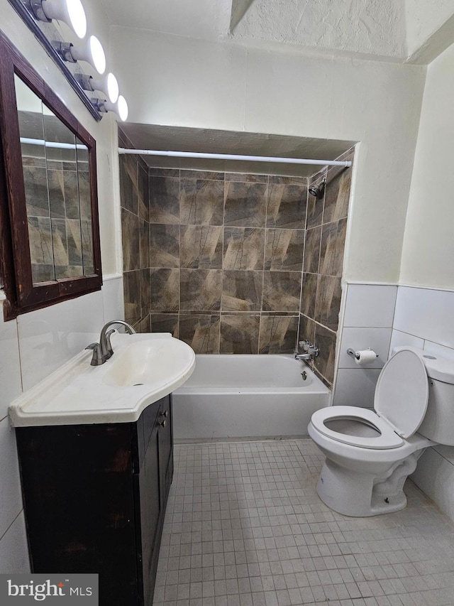 bathroom with tile patterned flooring, toilet, shower / bath combination, vanity, and tile walls