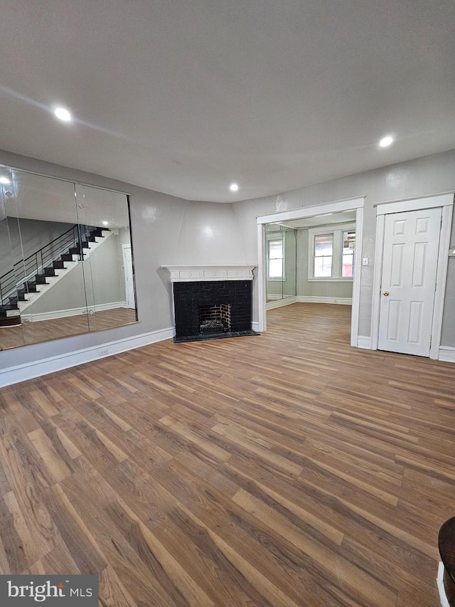 unfurnished living room with a fireplace, recessed lighting, wood finished floors, baseboards, and stairs