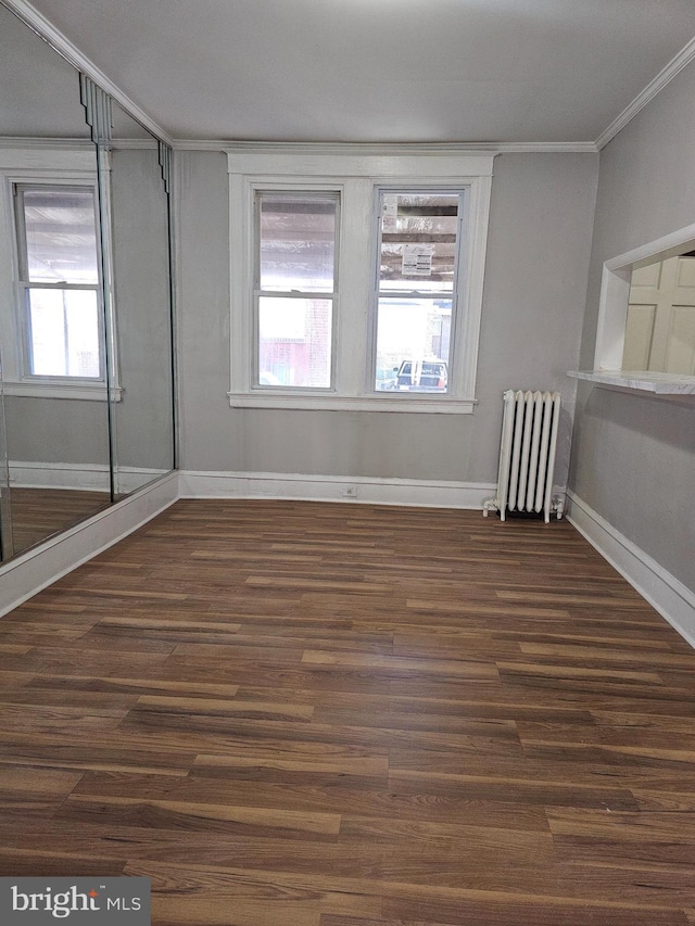 unfurnished room with crown molding, radiator heating unit, dark wood finished floors, and baseboards