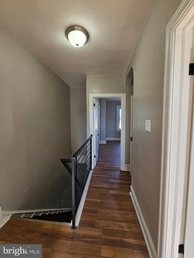 corridor featuring dark wood-style floors, baseboards, and arched walkways