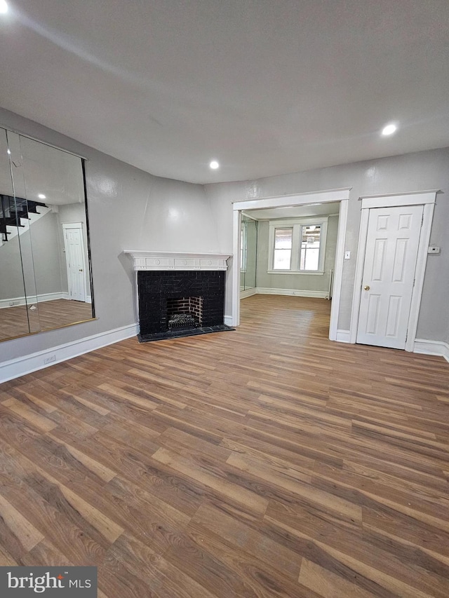 unfurnished living room featuring stairs, a fireplace, baseboards, and wood finished floors