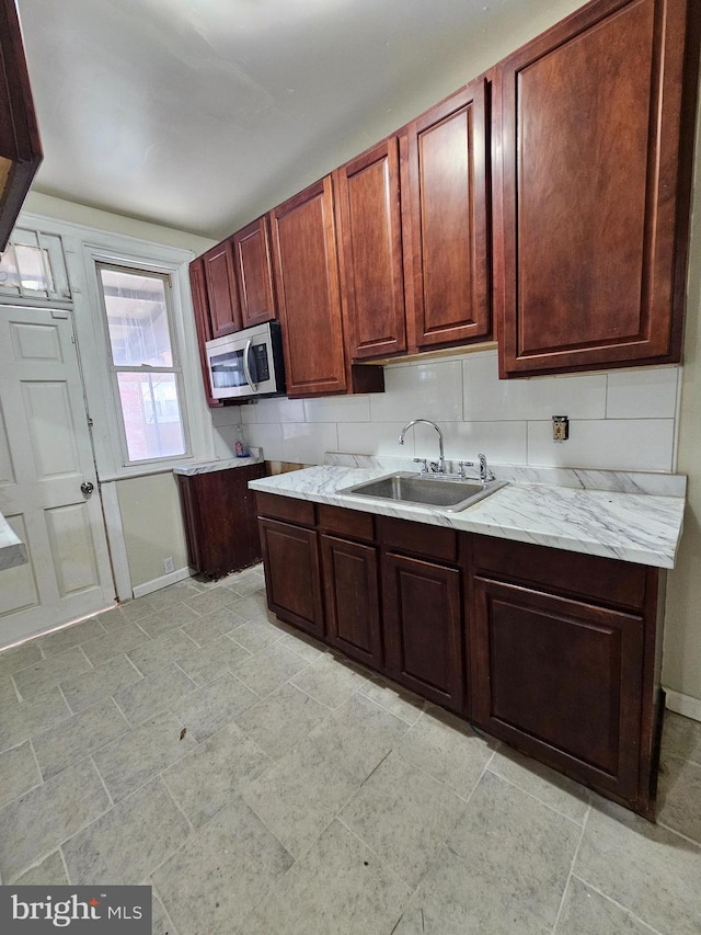 kitchen with baseboards, stainless steel microwave, decorative backsplash, and a sink