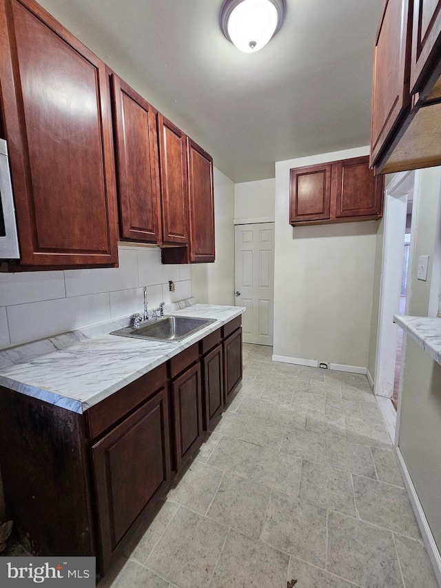 kitchen featuring a sink, baseboards, light countertops, backsplash, and stone finish flooring