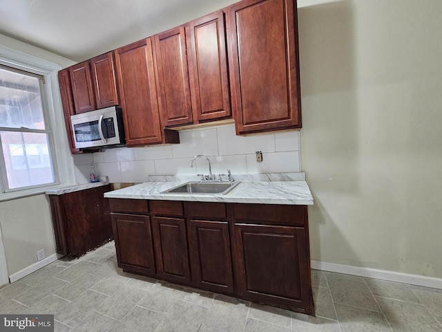 kitchen with baseboards, stainless steel microwave, backsplash, and a sink