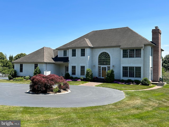 view of front of home with stucco siding, a front lawn, roof with shingles, and a chimney