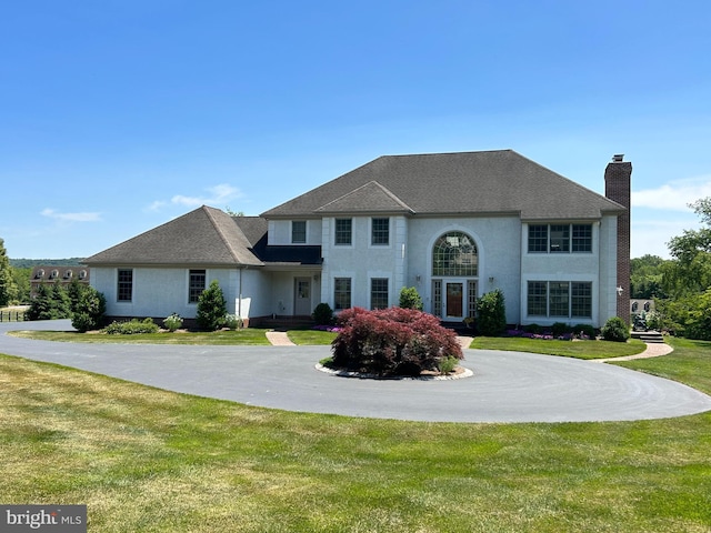 view of front facade with a front lawn, stucco siding, driveway, and a chimney