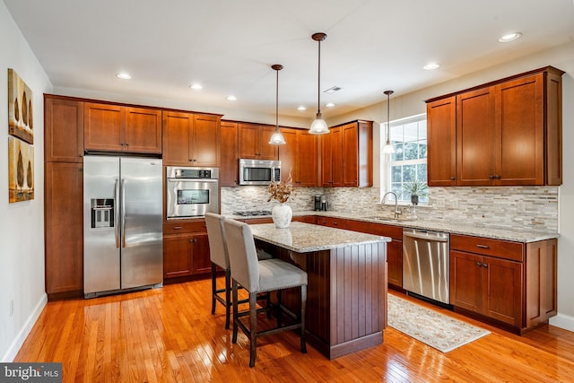 kitchen with a breakfast bar area, stainless steel appliances, backsplash, light wood-style flooring, and a sink