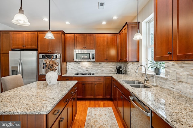 kitchen featuring stainless steel appliances, a sink, light stone countertops, light wood finished floors, and brown cabinetry