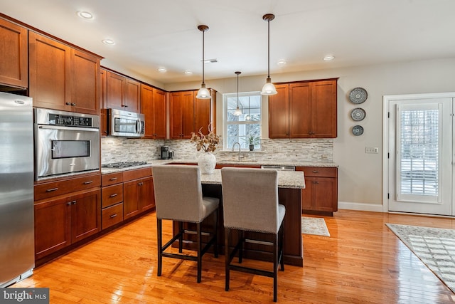 kitchen with light stone counters, a breakfast bar, decorative backsplash, appliances with stainless steel finishes, and light wood-type flooring