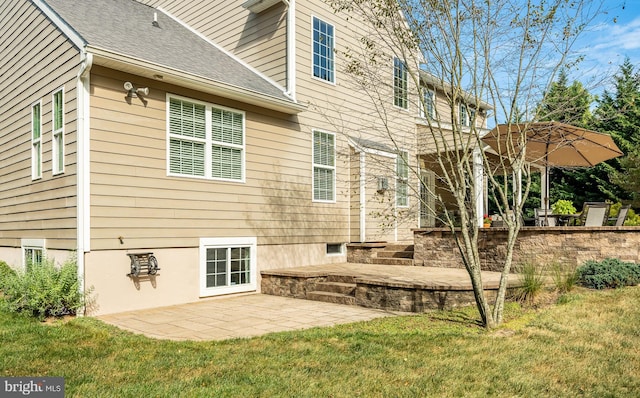 rear view of house featuring a shingled roof, a lawn, and a patio area