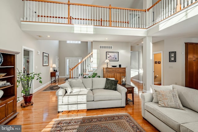 living room featuring light wood finished floors, baseboards, visible vents, a towering ceiling, and stairway