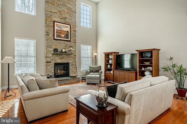 living area featuring baseboards, a high ceiling, a fireplace, and light wood finished floors